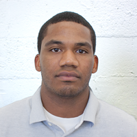 A young man standing in front of a white brick wall.